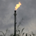 A tall industrial flare stack burning off gas against a gray, overcast sky