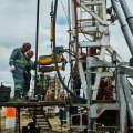 Several workers operating heavy machinery on an active oil or gas drilling site.
