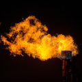 A large burst of bright orange flame coming from the top of an industrial flare stack against a completely dark background